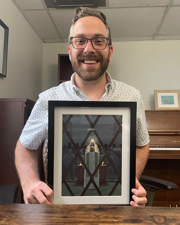 David Bibee holding an illustration from the Spring 2020 SCU Magazine, which hangs as a constant reminder of Christ’s call to serve the least of these.