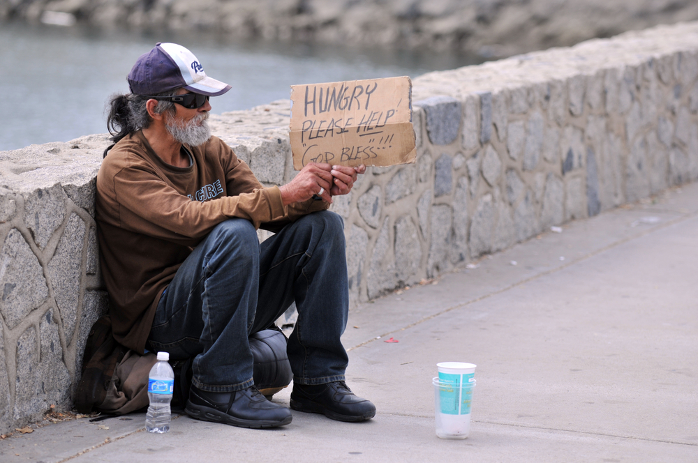 Homeless man holding sign that says 