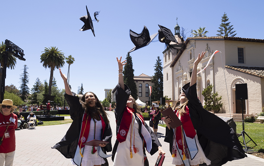 Three female graduates toss their caps in the air alongside Mission Church