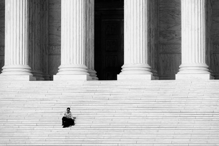 Man seated on expansive courthouse steps with columns behind him