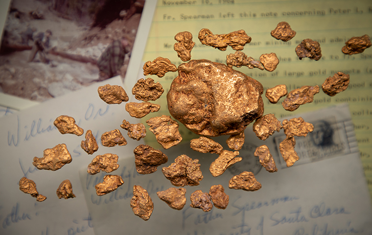 Gold Nuggets resting on top of a collage of letters, photos, and historical documents