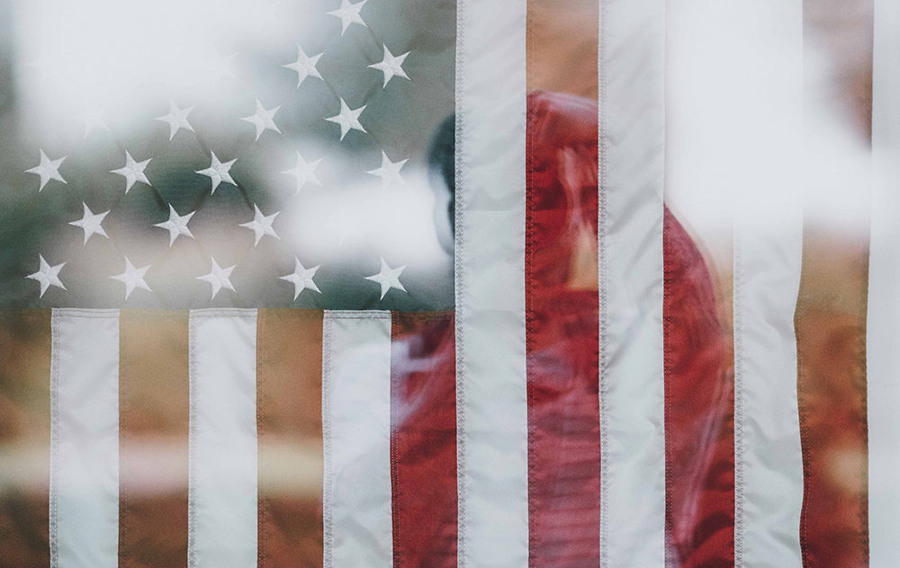 The reflection of a person in glass over an American flag