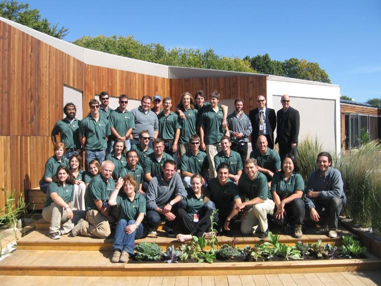 A large group of students wearing green shirts gather in front of the Solar Decathlon House 