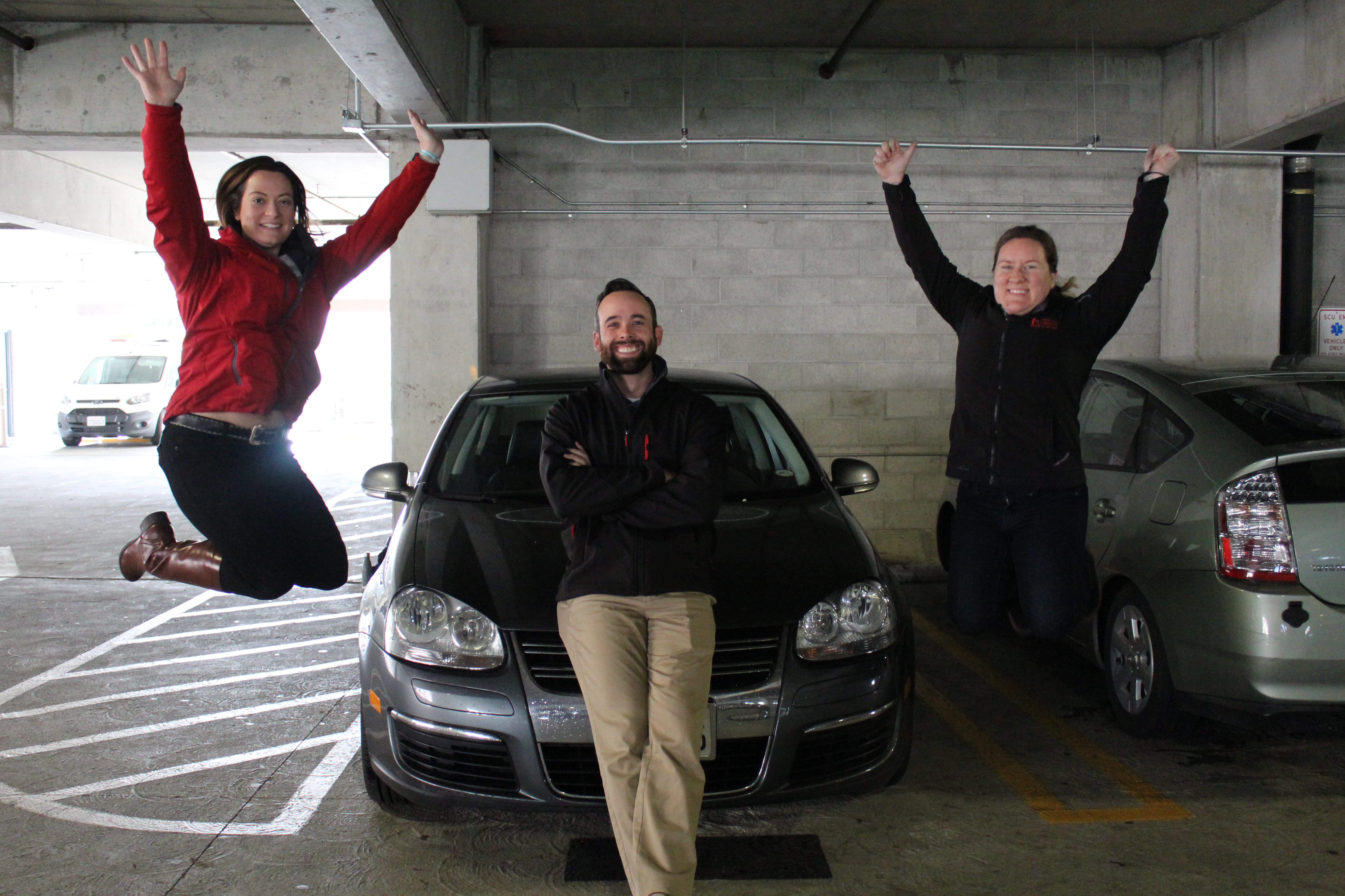 Three SCU employees who carpool together smile next to car