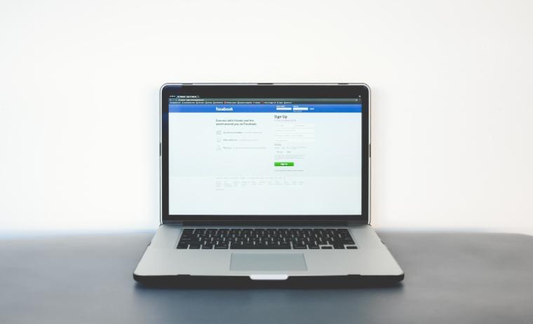 A laptop on a grey desk displaying the Facebook login page