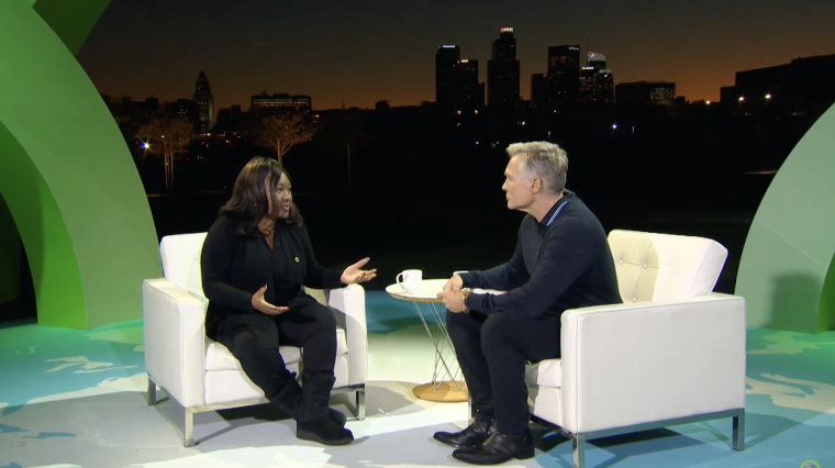 Activist Catherine Flowers sits with interviewer Sam Champion on a stage with a dark city skyline in the background