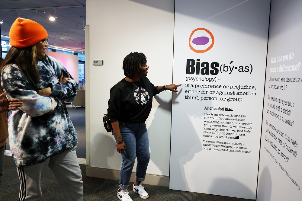 Two people looking at a wall featuring the definition of Bias image link to story