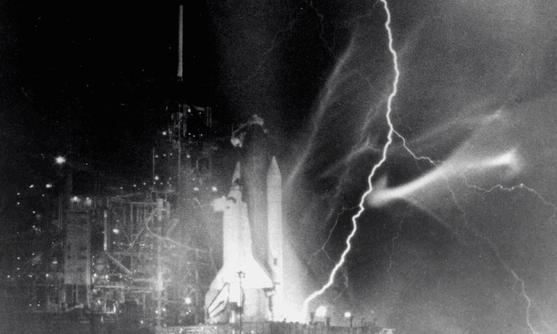 Lightning striking the ground at the base of a space ship, poised to launch
