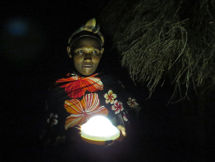 A Tanzanian woman holding a solar light outside in the dark