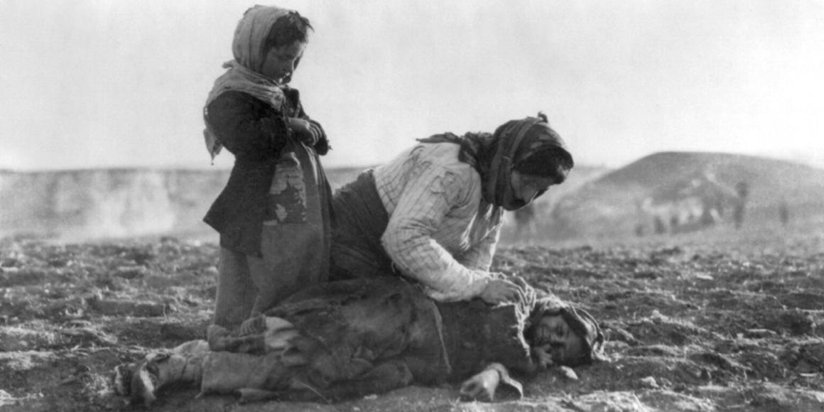 Historic photo of Armenian woman kneeling in a battllefield with two daughters.