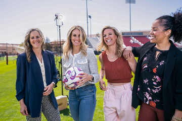 Four women standing together. One holds a soccer ball. 