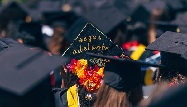 A sea of mortarboards, one decorated with segui adelante