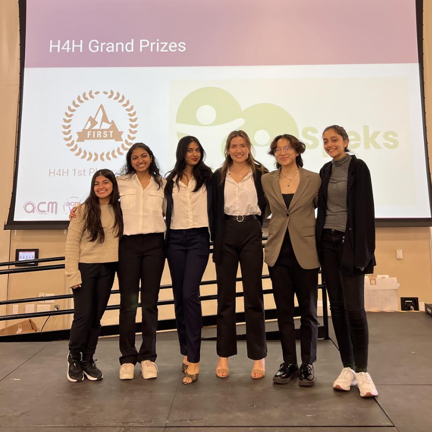 Six people standing together onstage with logos in the background, H4H Winners 23.