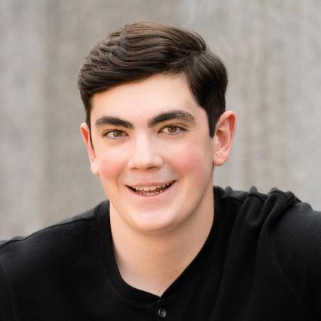 A person sitting against a wooden wall, wearing a black shirt and jeans.