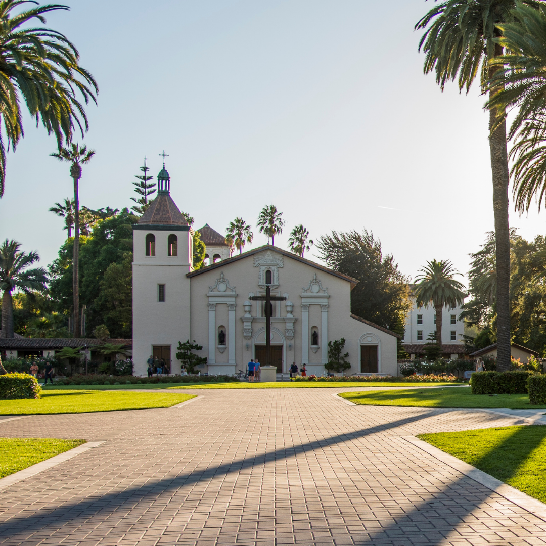 A pathway leading to a historic church surrounded by palm trees and greenery.