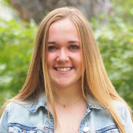 A person wearing a denim jacket over a pink floral dress outdoors.