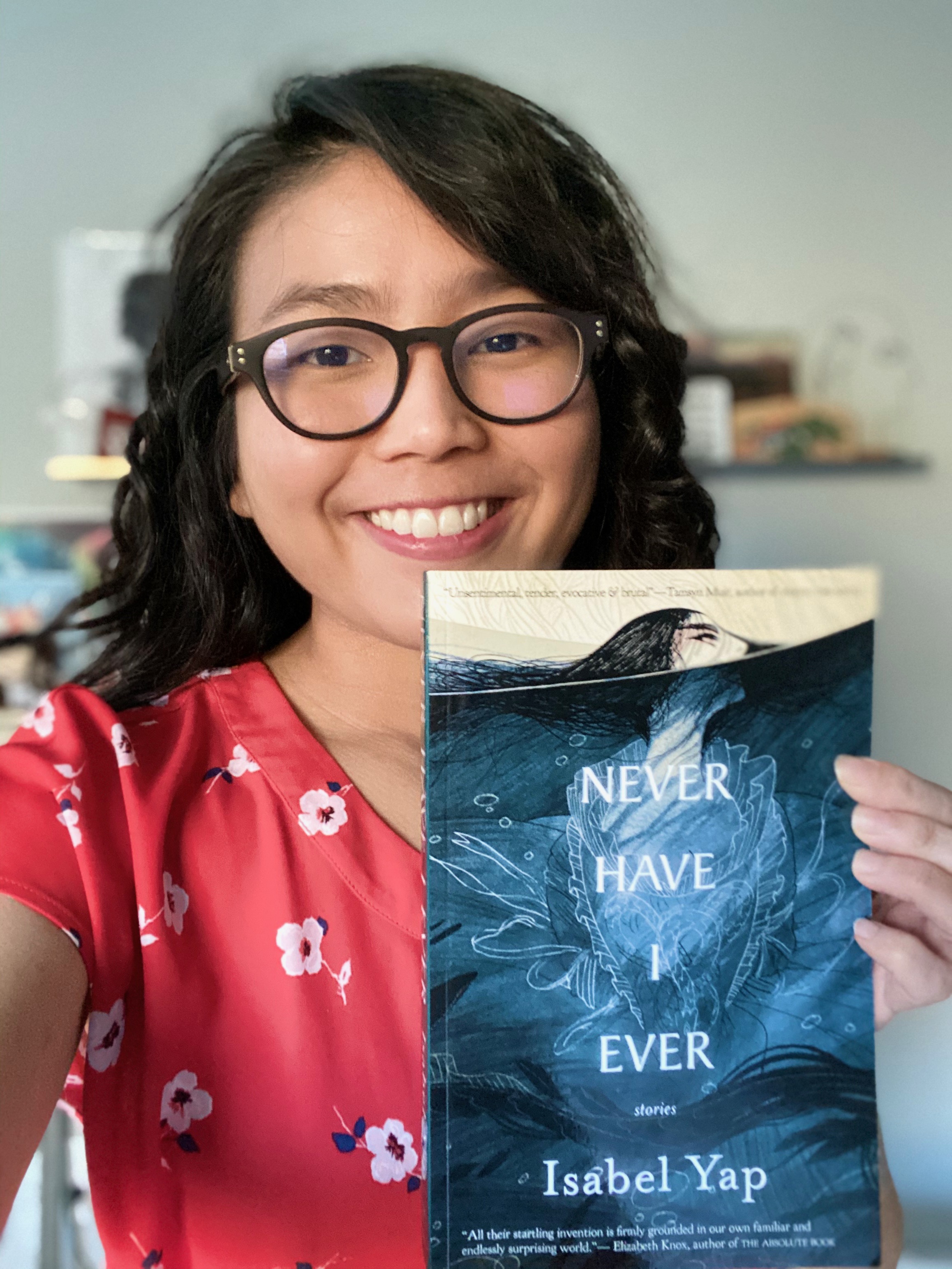 A person holding up a book titled Never Have I Ever by Isabel Yap.