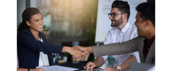 Three people around a table shaking hands during a discussion.