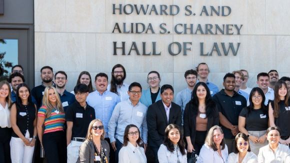 A group of smiling people in front of a Santa Clara University building labeled Howard S. and Alida S. Charney Hall of Law