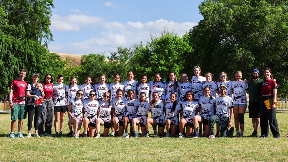 A posed group shot of 30 people. Most are young women, wearing white t-shirts emblazoned with the word Rage. The other men and women wear red shirts with the same Rage logo.