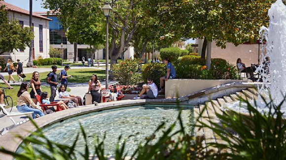 About a dozen smiling students sit by the fountain at Santa Clara Universitys Benson Center.