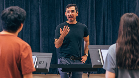 A man in casual clothing directs two students with music stands in front of them.