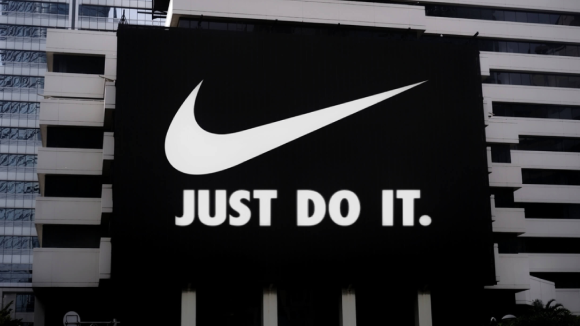 A black billboard with a white Nike brand swoosh and white text underneath, reading Just do it.