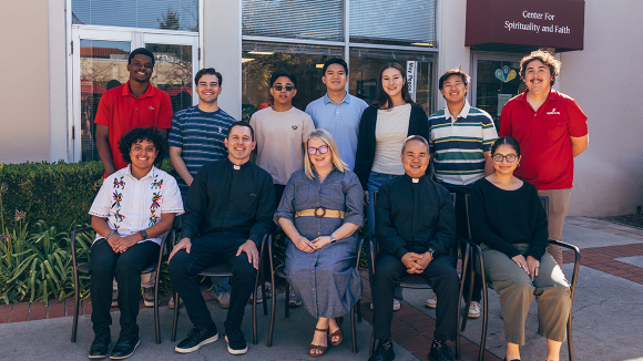 A smiling group of people posing in front of an office labeled Center for Spirituality and Faith.
