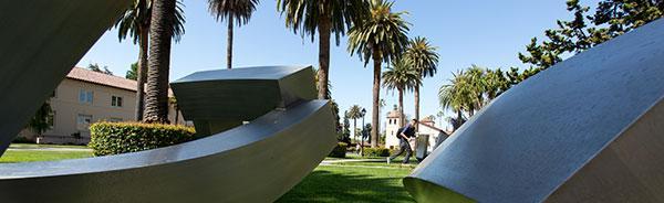 Cube sculpture in an outdoor park with palm trees.