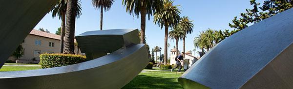 Cube sculpture in an outdoor park with palm trees.