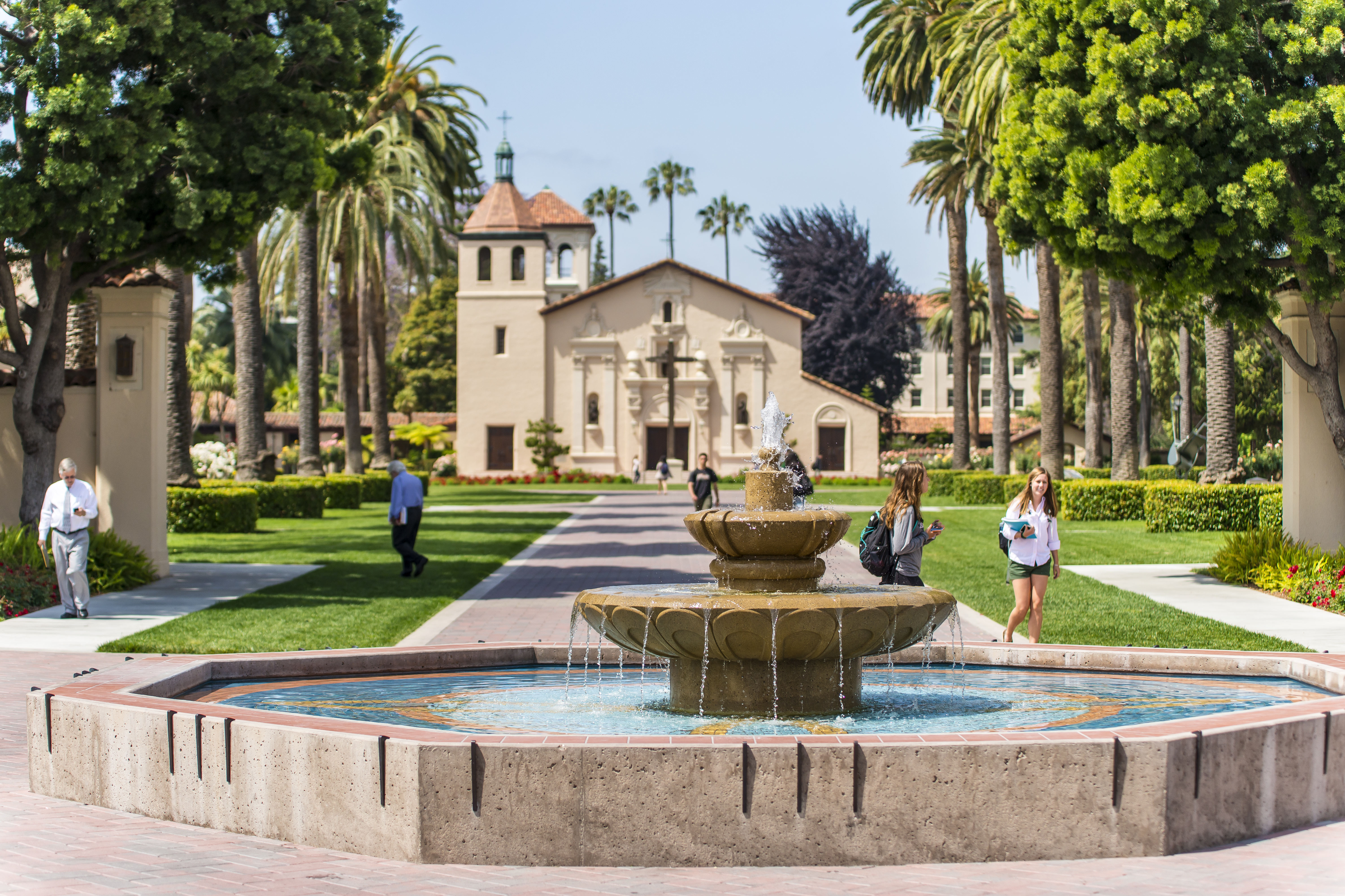 Students walk next to a fountain with the Santa Clara Mission Church visible in the background.