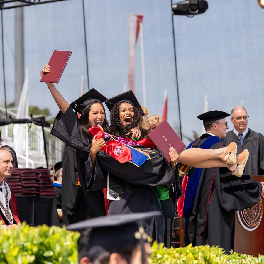 Class of 2025 alumni holds up a fellow classmate onstage at commencement 