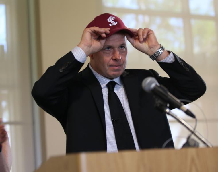 A person adjusts a cap while speaking at a podium. image link to story