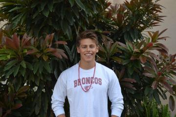A person wearing a Stanford sweatshirt stands in front of plants.
