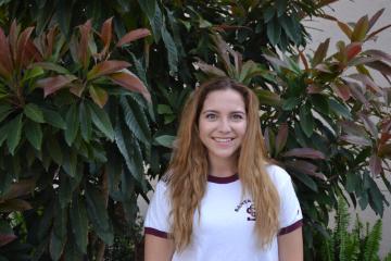 A person smiling in front of green plants.