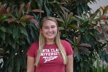 A person in a red shirt standing in front of green plants.