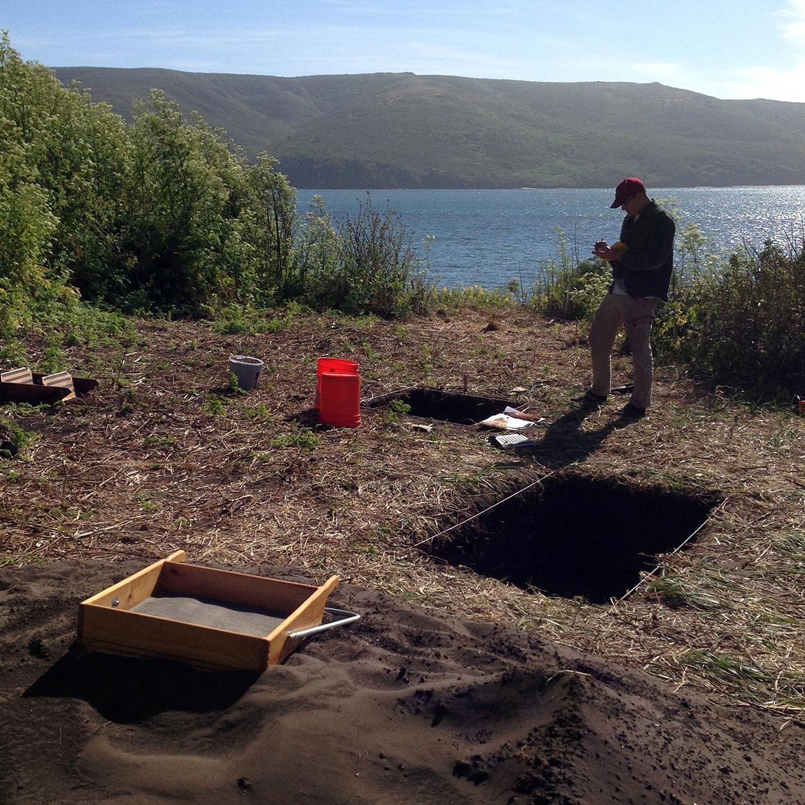 A person excavating near dug pits with a lake in the background. image link to story