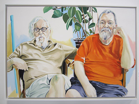 Two people sitting; one in a beige outfit, the other in an orange shirt.