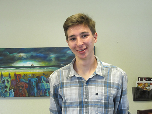 A person in a plaid shirt smiling in front of a painting.