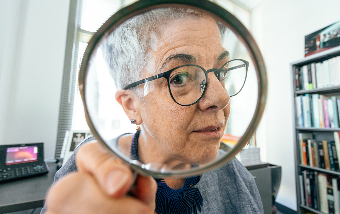 Andrea Pappas in an office with bookshelves peering through a magnifying glass at the camera image link to story