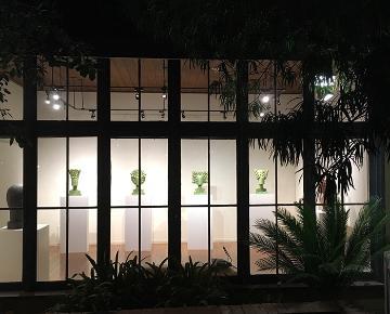 Exterior view of a building with art displays and plants at night. image link to story
