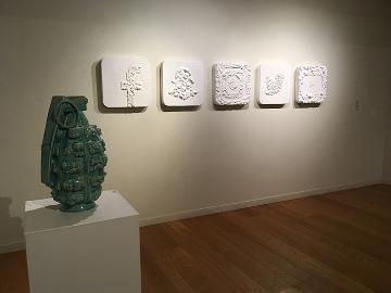 A piece of pottery on a pedestal and framed artworks on a gallery wall.