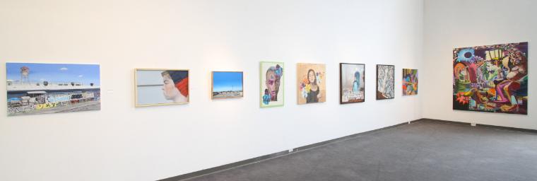 A gallery wall displaying various paintings and photographs in an exhibition.