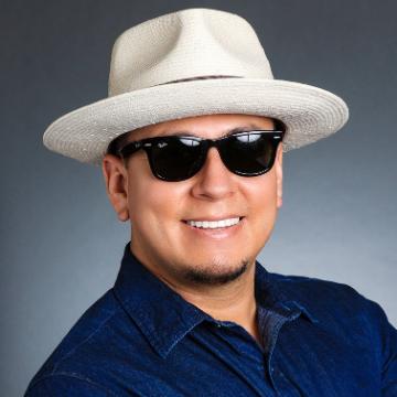 A person wearing sunglasses and a white hat smiles at the camera.