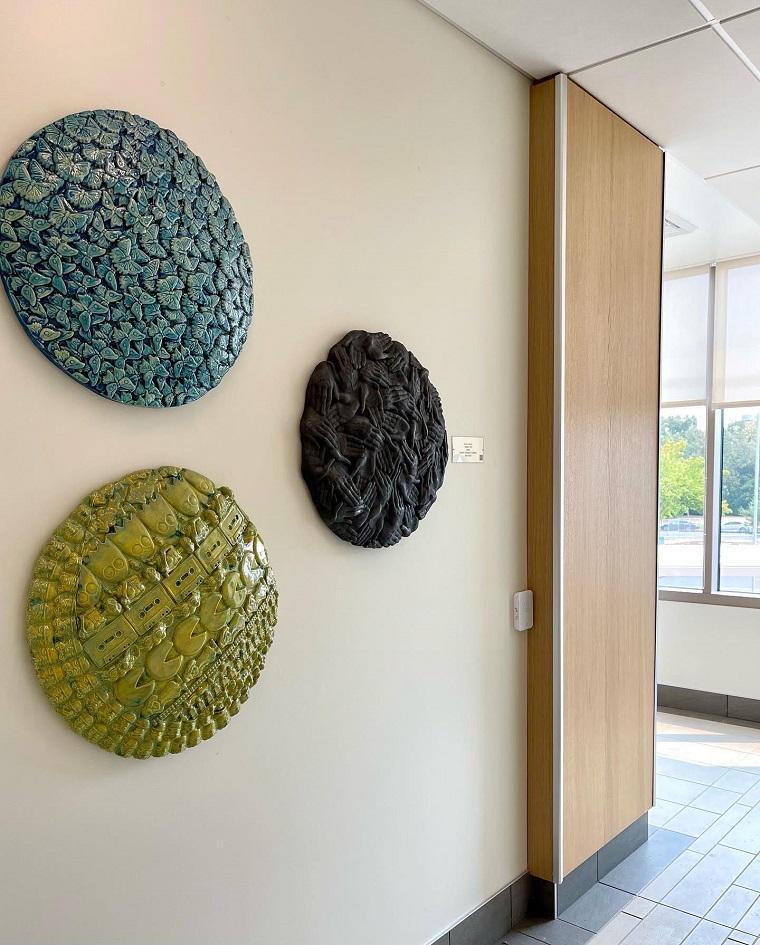 Three circular ceramic art pieces in blue, black, and green displayed on a wall. image link to story