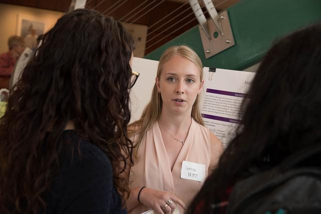 Three people having a conversation near a poster titled 