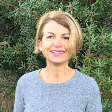 A woman smiling in front of greenery.