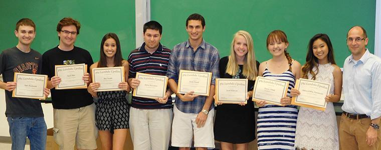 A group of students holding awards in front of a green chalkboard. image link to story