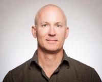 A man in a dark shirt against a plain background.