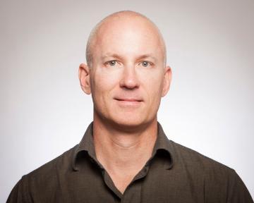 A man in a dark shirt against a plain background. image link to story